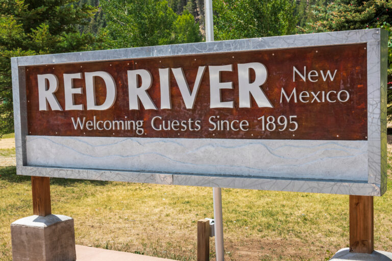 Welcome sign reading Red River, New Mexico, Welcoming Guests Since 1895, with pine trees behind