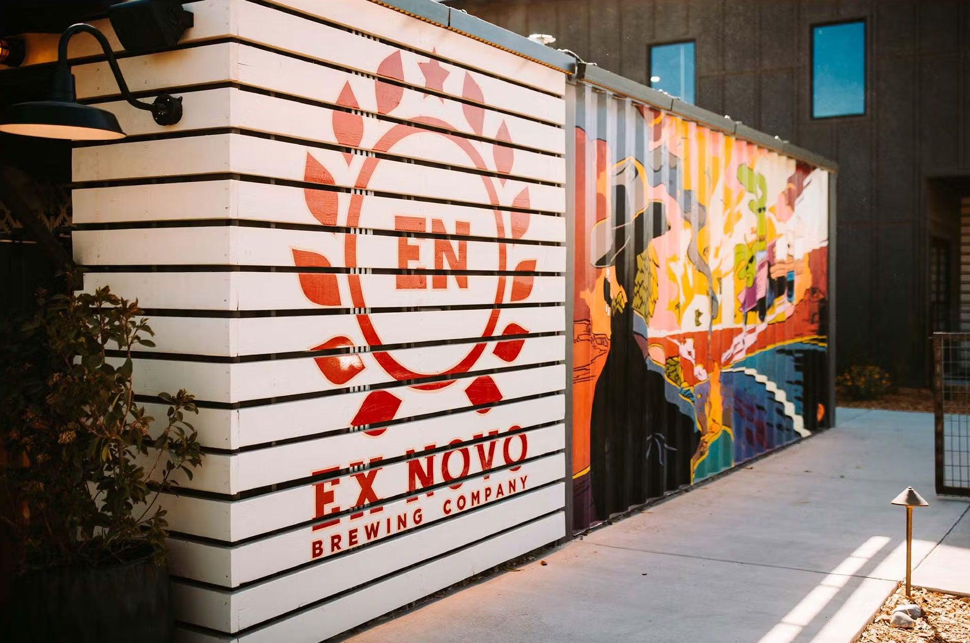 Ex Novo Brewing Company sign on a white slatted wall beside a colorful painted mural, in afternoon light