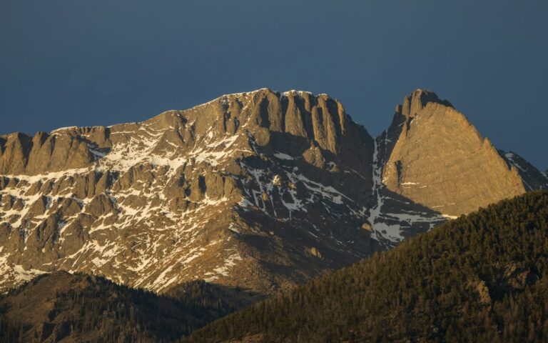 Snow-streaked granite peaks of the Sangre de Cristo Mountains in late-day light above forested ridges