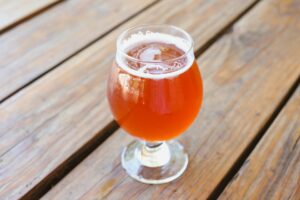 A reddish-amber sour beer in a stemmed tulip glass on a wooden picnic table