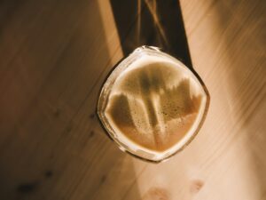 Overhead view of a glass of dark stout with a creamy tan head on a sunlit wooden table