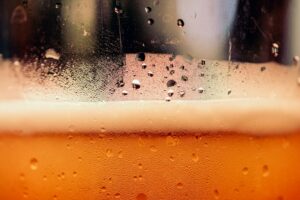 Close-up of a cold amber beer with a white foam head in a frosted glass.