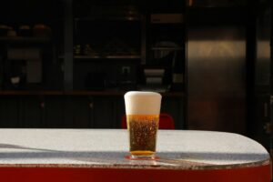 A pint glass of pale golden lager with a thick white head on a sunlit table