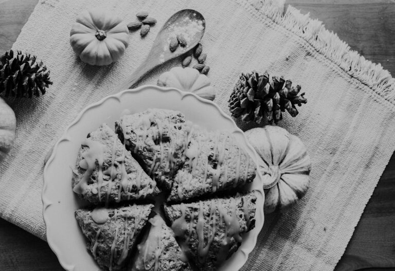 Glazed pumpkin scones on a white plate with small pumpkins and pine cones, in black and white